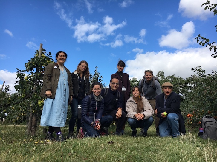 A group photo of 8 people standing in an apple orchard against a blue sky