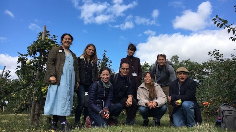 A group photo of 8 people standing in an apple orchard against a blue sky