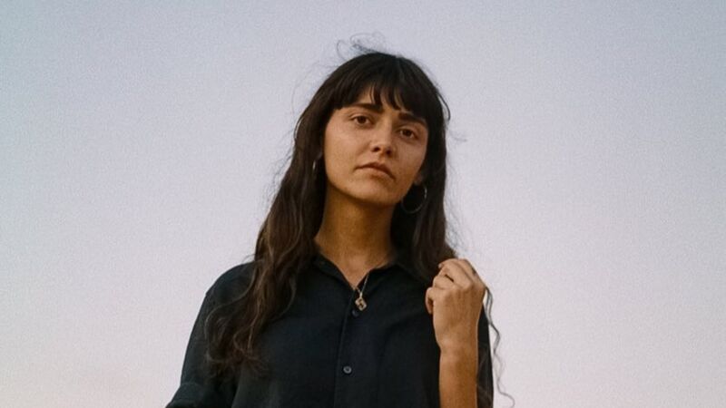 A portrait of Zsuzsanna Ihar, with long dark hair standing against a pale sky