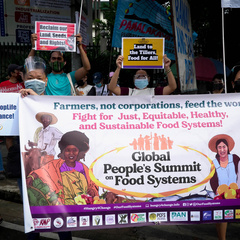 A crowd of protesters carry banners reading "Farmers, not corporations, feed the world. Fight for just, equitable, healthy and sustainable food systems!"