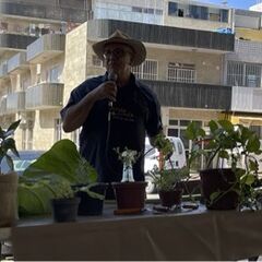 A man stands at a market stall, speaking into a microphone 
