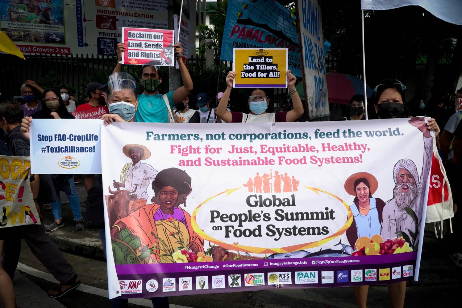 A crowd of protesters carry banners reading "Farmers, not corporations, feed the world. Fight for just, equitable, healthy and sustainable food systems!"